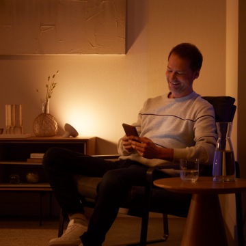 Een man ontspant op een stoel, omgeven door warmwitte, slimme Philips Hue verlichting.