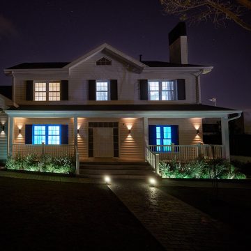 A home seen from the outside showing the doorway, entrance, and rooms inside the house lit with bright white light for added home security.