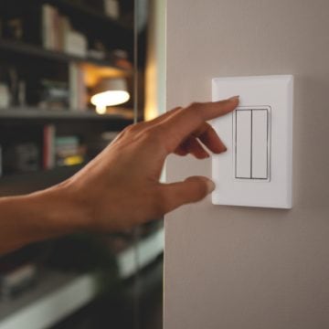 Dłoń, która lada chwila obróci biały naścienny inteligentny przełącznik oświetlenia