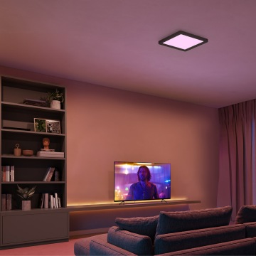 Czarna, kwadratowa lampa sufitowa ustawiona na fioletowe światło w salonie z telewizorem