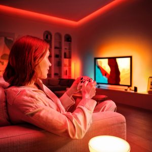 Uma mulher joga videogame e você pode ver uma iluminação envolvente na parede atrás da TV.